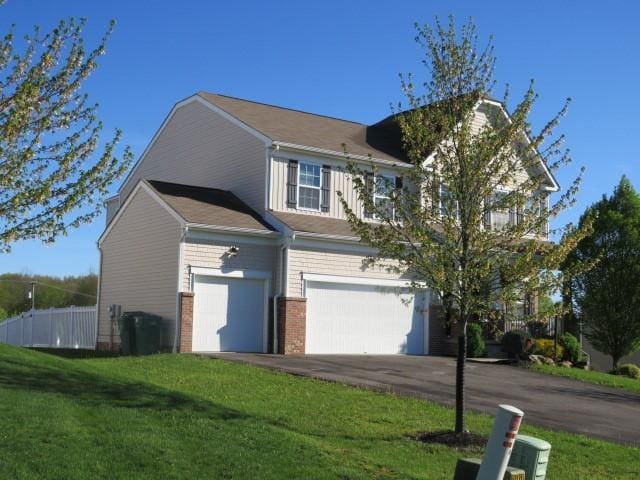 view of side of home featuring driveway, brick siding, a lawn, and an attached garage