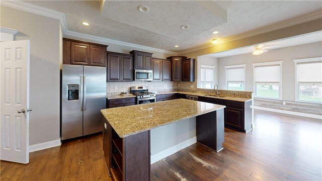 kitchen featuring stainless steel appliances, a center island, dark brown cabinetry, dark wood-type flooring, and light stone counters