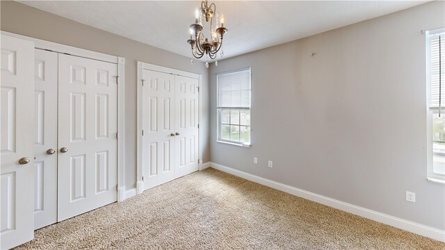 unfurnished bedroom featuring two closets, carpet floors, a chandelier, and baseboards