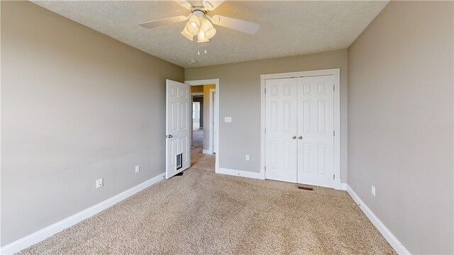 unfurnished bedroom featuring light carpet, a closet, baseboards, ceiling fan, and a textured ceiling