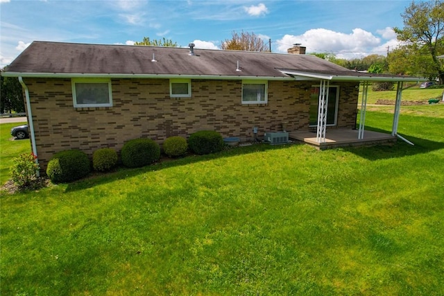 rear view of house with cooling unit, a chimney, a lawn, and brick siding
