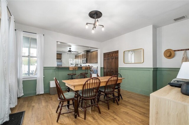 dining room with a wainscoted wall, light wood-type flooring, and ceiling fan