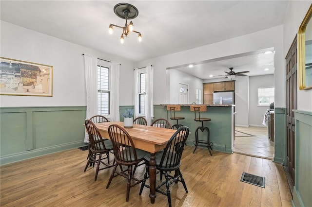 dining space featuring plenty of natural light, light wood finished floors, a wainscoted wall, a ceiling fan, and a decorative wall