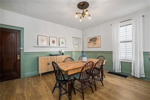 dining space with a chandelier, wainscoting, and wood finished floors