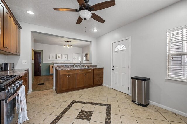 kitchen with stainless steel range with gas stovetop, ceiling fan, a sink, light tile patterned floors, and a peninsula