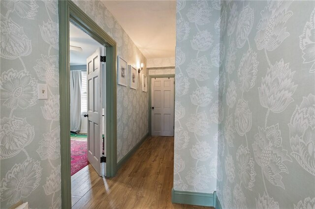 corridor featuring wood finished floors, wallpapered walls, and baseboards