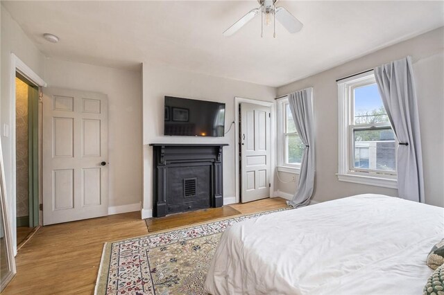 bedroom with wood finished floors, baseboards, a fireplace with flush hearth, and ceiling fan