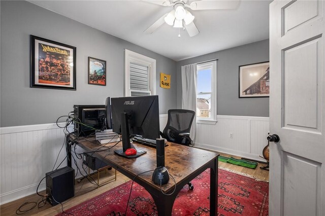office space featuring wood finished floors, wainscoting, and a ceiling fan