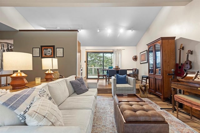 living room featuring track lighting, light wood-type flooring, and vaulted ceiling