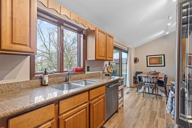 kitchen with a sink, vaulted ceiling, stainless steel dishwasher, light wood-type flooring, and light stone counters