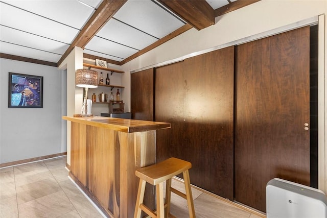 indoor bar featuring baseboards and beamed ceiling