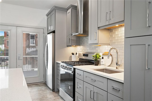 kitchen with stainless steel appliances, gray cabinets, a sink, wall chimney exhaust hood, and tasteful backsplash