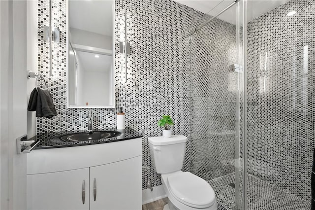 full bath featuring toilet, a stall shower, vanity, and tile walls