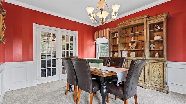 carpeted dining area featuring french doors, a chandelier, wainscoting, crown molding, and a decorative wall