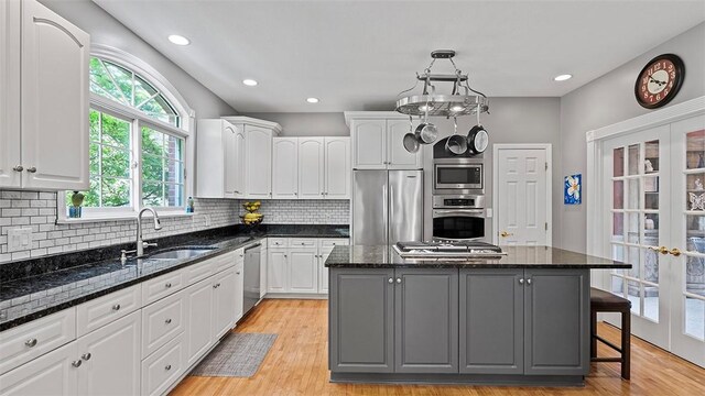 kitchen featuring stainless steel appliances, a sink, gray cabinets, a center island, and white cabinetry
