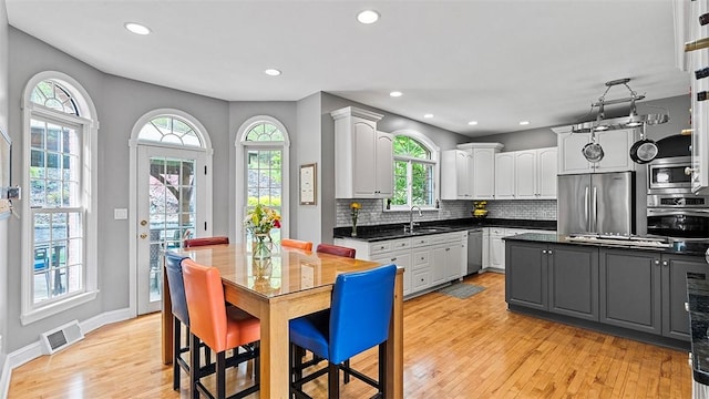kitchen featuring appliances with stainless steel finishes, a sink, dark countertops, light wood finished floors, and tasteful backsplash