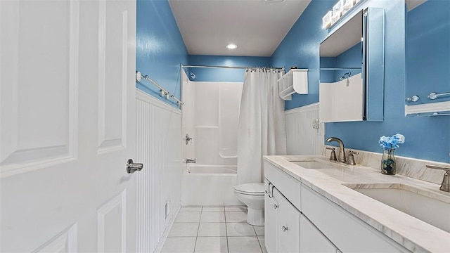 full bath with tile patterned floors, toilet, double vanity, shower / bath combination with curtain, and a wainscoted wall