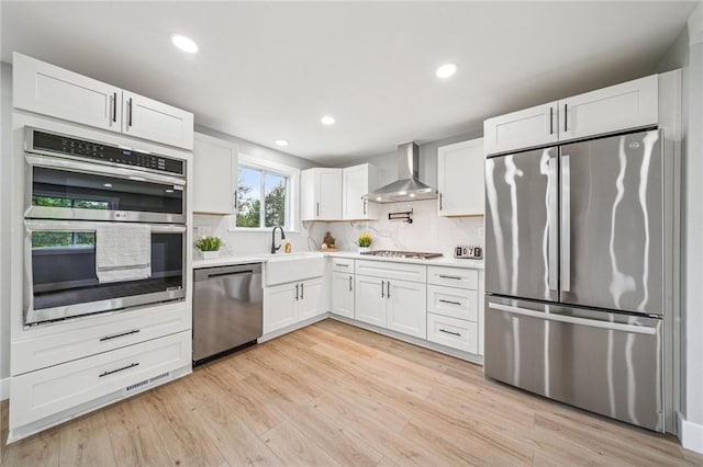 kitchen featuring appliances with stainless steel finishes, wall chimney range hood, light countertops, tasteful backsplash, and recessed lighting