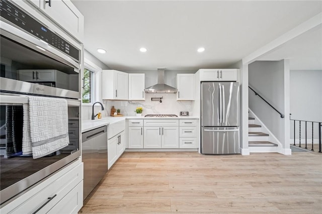kitchen with stainless steel appliances, wall chimney range hood, white cabinetry, light wood-type flooring, and recessed lighting