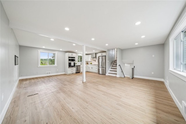 basement featuring freestanding refrigerator, light wood finished floors, baseboards, stairway, and recessed lighting