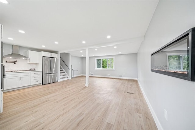 unfurnished living room with stairway, light wood-style floors, baseboards, and recessed lighting