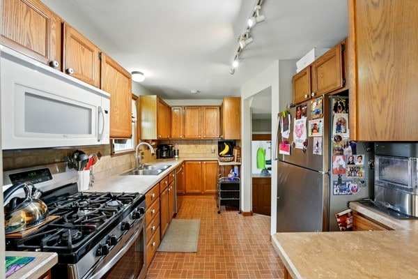 kitchen with appliances with stainless steel finishes, a sink, backsplash, and light countertops