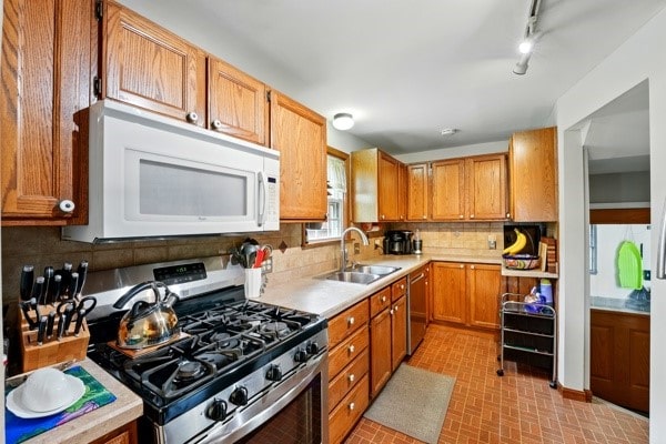 kitchen featuring stainless steel appliances, a sink, light countertops, decorative backsplash, and brick patterned floors