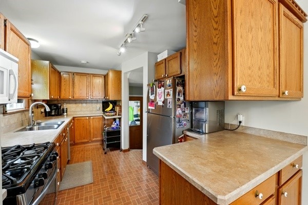 kitchen featuring a sink, gas range oven, freestanding refrigerator, tasteful backsplash, and light countertops