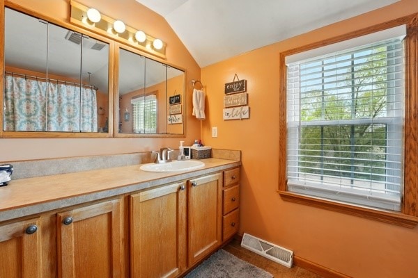 bathroom featuring plenty of natural light, vaulted ceiling, vanity, tile patterned floors, and baseboards