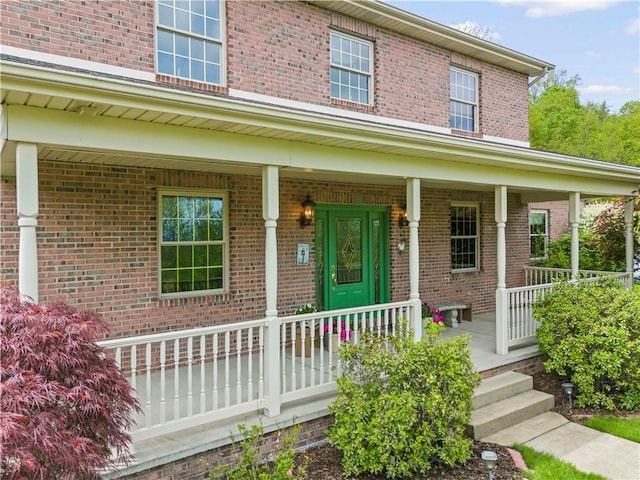 view of exterior entry with a porch and brick siding