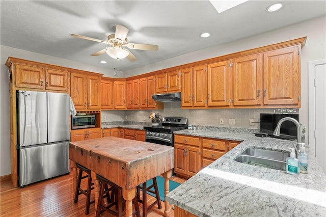 kitchen featuring stainless steel appliances, a sink, under cabinet range hood, light wood-type flooring, and ceiling fan
