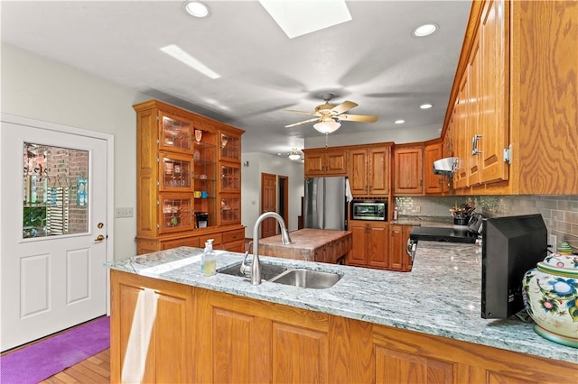 kitchen with a sink, stainless steel appliances, brown cabinetry, a peninsula, and recessed lighting
