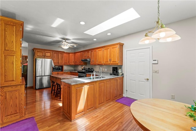 kitchen with stainless steel appliances, a sink, a peninsula, a skylight, and light wood-style flooring