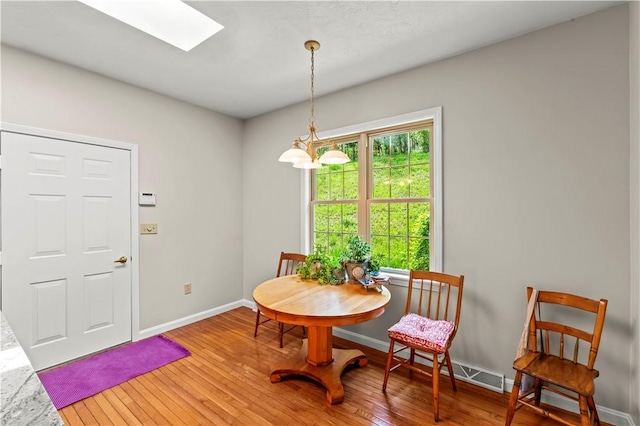 dining area with hardwood / wood-style flooring, a skylight, and baseboards