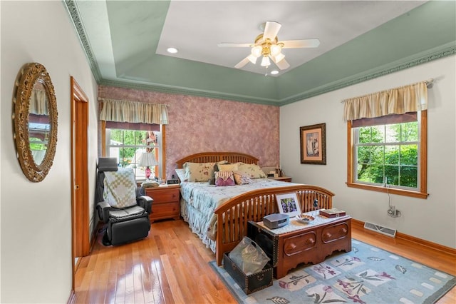 bedroom with a tray ceiling, wood-type flooring, baseboards, and a ceiling fan
