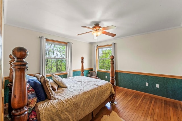 bedroom with hardwood / wood-style flooring, baseboards, crown molding, ceiling fan, and a wainscoted wall