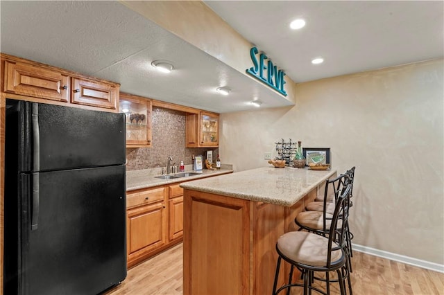 kitchen featuring freestanding refrigerator, a sink, a kitchen bar, light wood finished floors, and recessed lighting