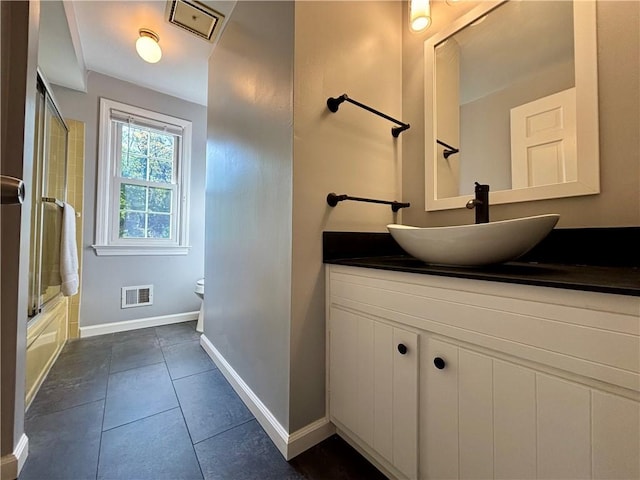 bathroom with baseboards, tile patterned floors, shower / bath combination with glass door, vanity, and toilet
