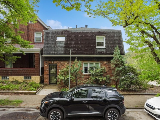 view of front of property featuring mansard roof, a shingled roof, and brick siding