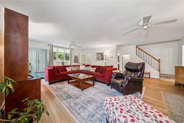 living area featuring ceiling fan, light wood-type flooring, stairway, and baseboards