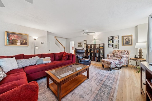 living room with a ceiling fan, light wood-style floors, and stairs