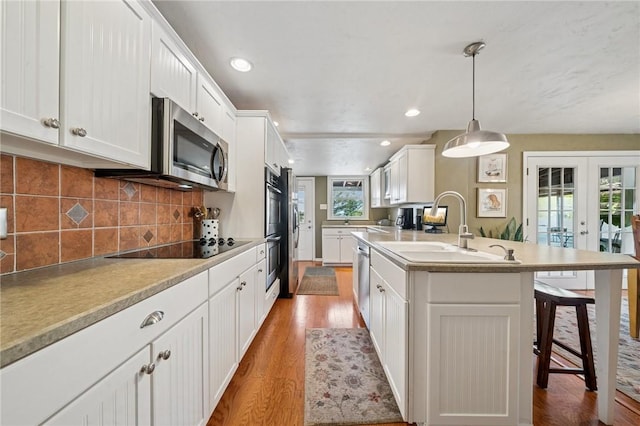 kitchen featuring stainless steel appliances, a sink, wood finished floors, a kitchen breakfast bar, and french doors
