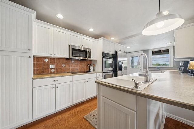 kitchen featuring appliances with stainless steel finishes, white cabinets, decorative backsplash, light wood-style floors, and a sink