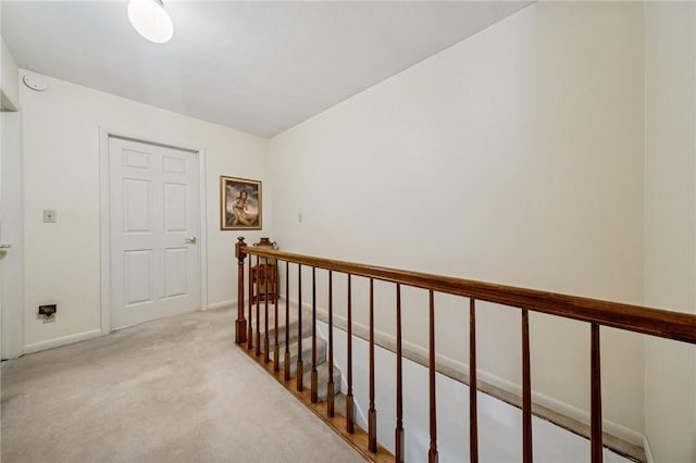 corridor with an upstairs landing, light carpet, and baseboards