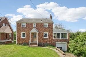 view of front of property featuring an attached garage, a front yard, a chimney, and brick siding