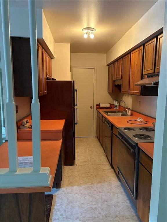 kitchen with a sink, black appliances, under cabinet range hood, and light flooring
