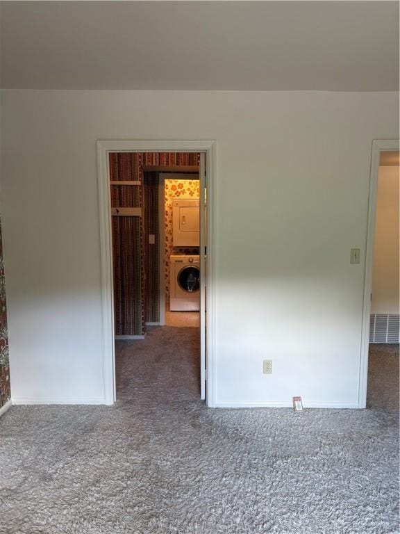 carpeted empty room featuring stacked washer / drying machine and baseboards