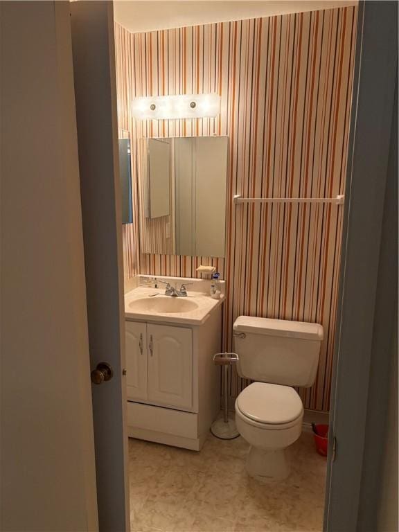 half bathroom featuring toilet, wallpapered walls, and vanity