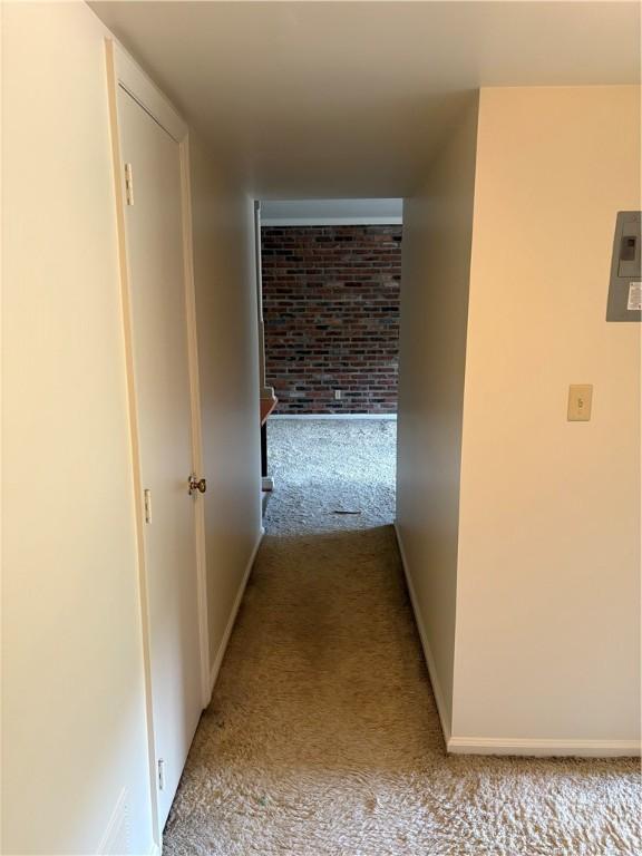 hall with carpet floors, baseboards, electric panel, and brick wall