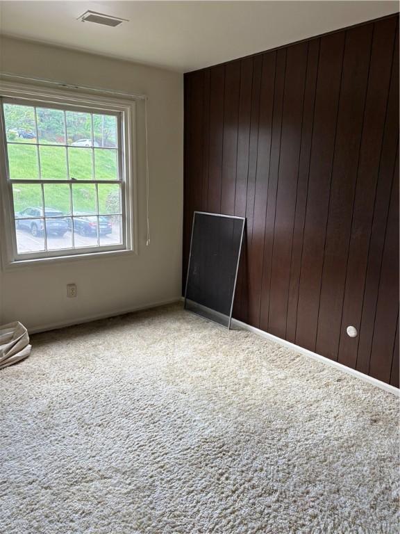 unfurnished room featuring carpet, wooden walls, and baseboards
